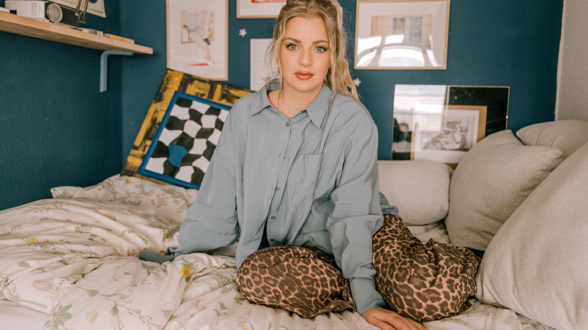 Laura Larsson in grauer Bluse und Leo-Hose auf einem Bett