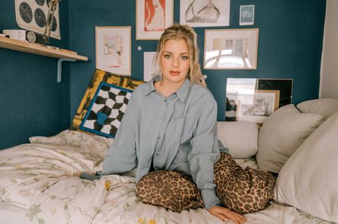 Laura Larsson in grauer Bluse und Leo-Hose auf einem Bett