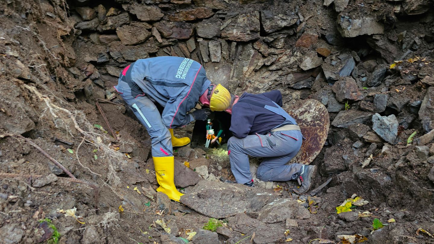 Zwei Männer in Arbeitskleidung beugen sich über die Öffnung eines alten Bergwerksstollens im Erzgebirge