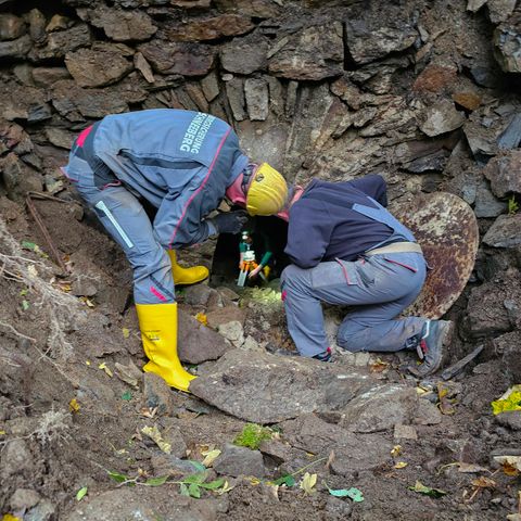 Zwei Männer in Arbeitskleidung beugen sich über die Öffnung eines alten Bergwerksstollens im Erzgebirge