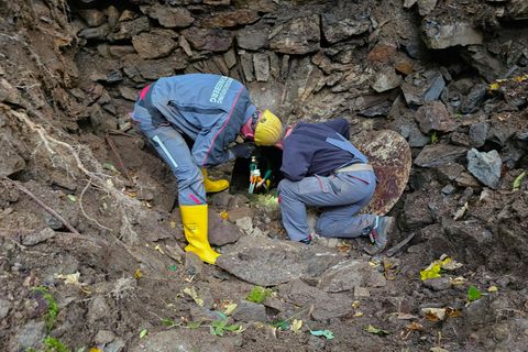 Zwei Männer in Arbeitskleidung beugen sich über die Öffnung eines alten Bergwerksstollens im Erzgebirge