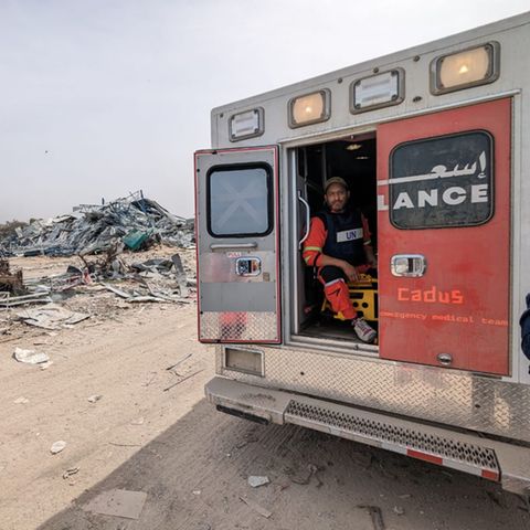 An ambulance from the Berlin aid organization Cadus in front of a destroyed backdrop in Gaza