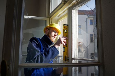 Ein Bauarbeiter mit gelbem Helm prüft mit Wasserwaage ein Fenster