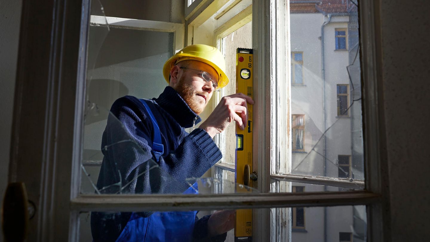 A construction worker with gelbem Helm prüft with Wasserwaage and Fenster