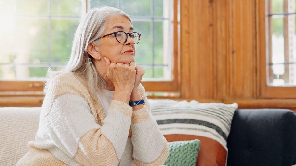 Mangelnde Selbstfürsorge: Eine ältere Frau sitzt nachdenklich auf dem Sofa