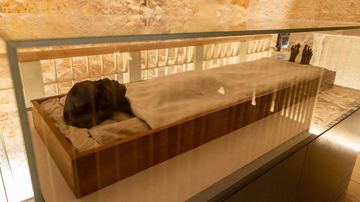 Mumie des Tutanchamun in einem Holzsarkophag unter weißem Tuch, nur Kopf und Füße sind zu sehen