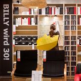 Eine Frau steht in einem Ikea vor Billy-Regalen, über der Schulter trägt sie eine gelbe Ikea-Tasche