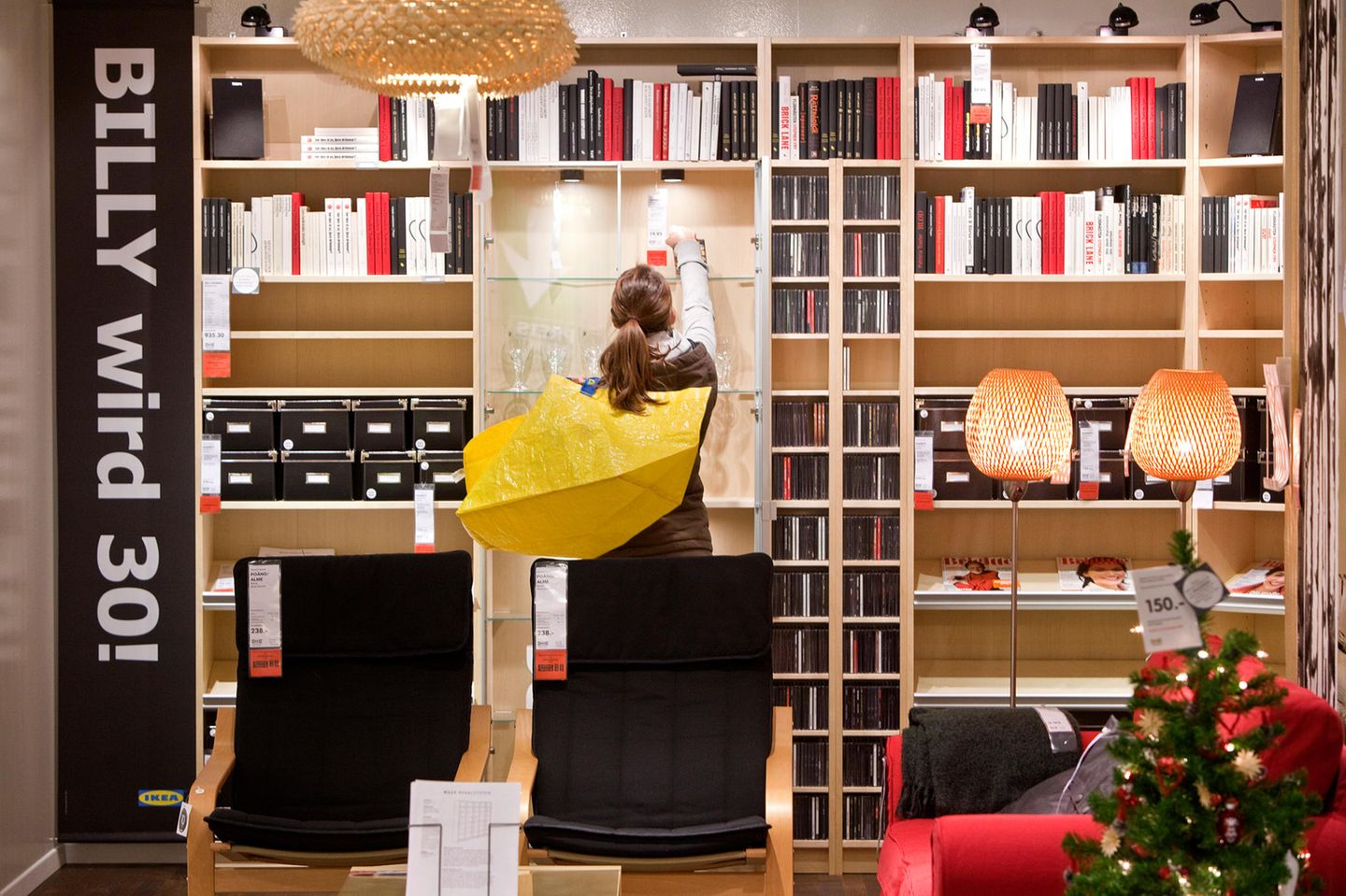 Eine Frau steht in einem Ikea vor Billy-Regalen, über der Schulter trägt sie eine gelbe Ikea-Tasche