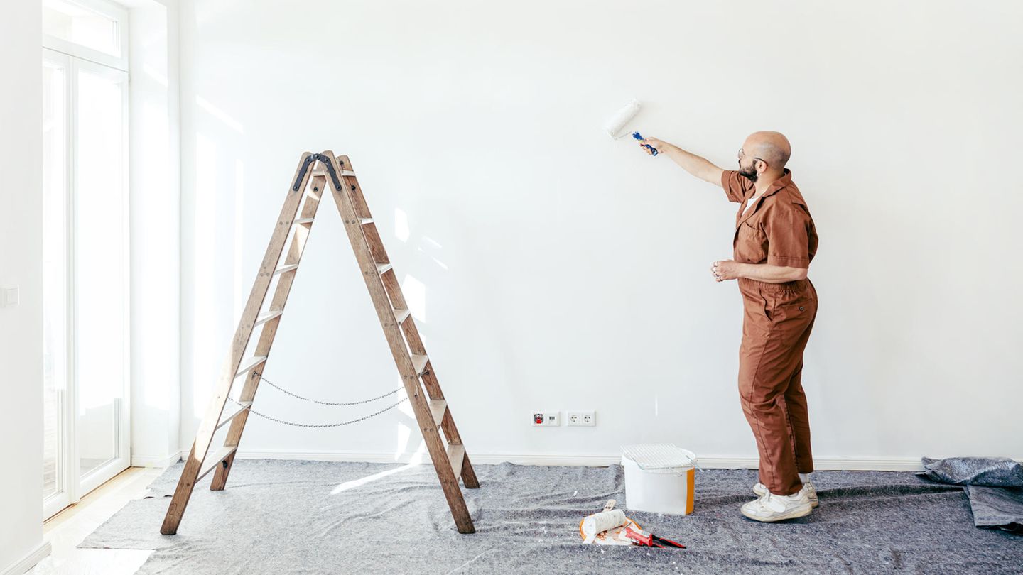 Ein Maler steht in einer leeren Wohnung und streicht die Wand