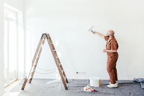 Ein Maler steht in einer leeren Wohnung und streicht die Wand
