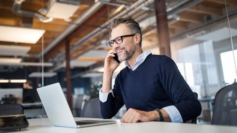 Vodafone Business: Geschäftsmann sitzt vor einem aufgeklappten Laptop und telefoniert mit dem Handy.