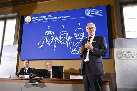 Drei Männer stehen vor einem Bildschirm, um den Nobelpreis zu vergeben.