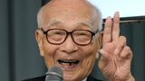 Terumi Tanaka spricht während einer Pressekonferenz und zeigt das Peace-Zeichen