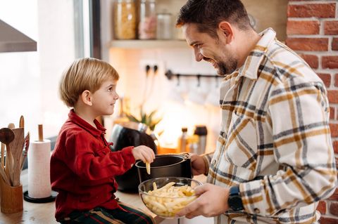 Vater bietet seinem Sohn Pommes aus der Heißluftfritteuse an.