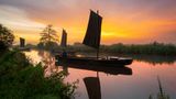Drei Kähne fahren bei Sonnenaufgang durch einen Kanal im Teufelsmoor