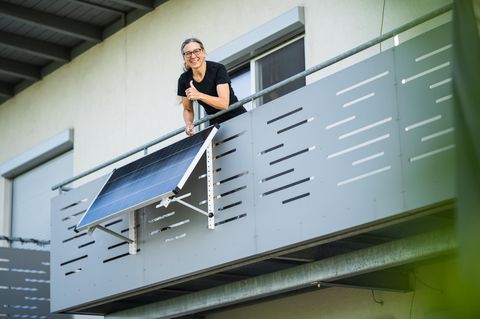 Frau posiert mit Daumen nach oben vor einem Balkonkraftwerk.