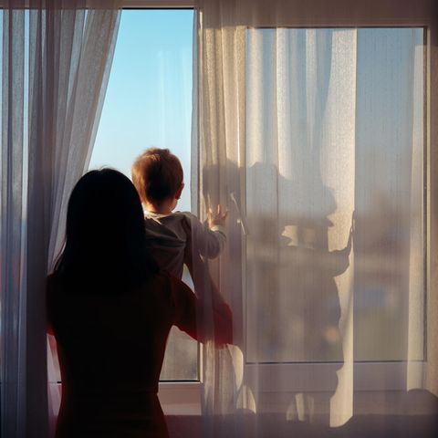 Symbolbild Regretting Motherhood: Eine Mutter guckt mit ihrem Baby aus dem Fenster