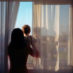 Symbolbild Regretting Motherhood: Eine Mutter guckt mit ihrem Baby aus dem Fenster