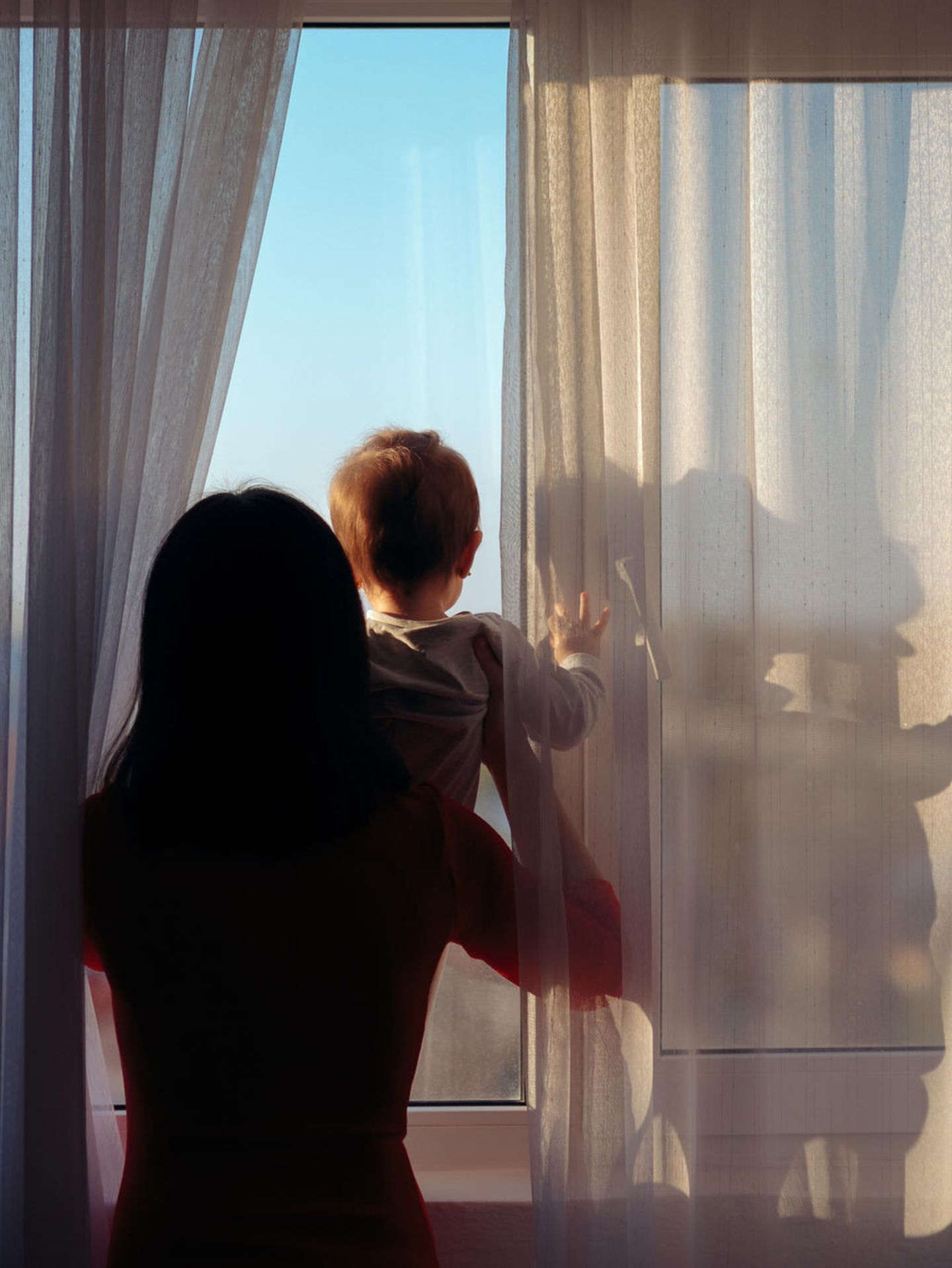 Symbolbild Regretting Motherhood: Eine Mutter guckt mit ihrem Baby aus dem Fenster