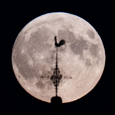 Ein Supermond hinter dem Wetterhahn einer Kirche