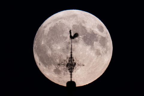 Ein Supermond hinter dem Wetterhahn einer Kirche