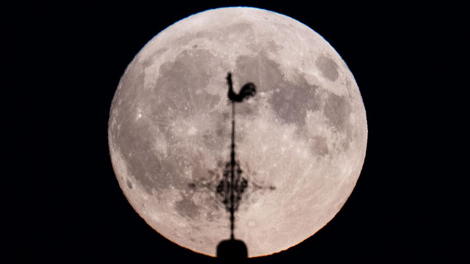 Ein Supermond hinter dem Wetterhahn einer Kirche