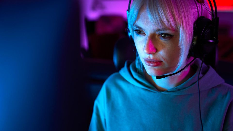 Eine junge Frau sitzt vor einem Bildschirm mit Kopfhörern und spielt League