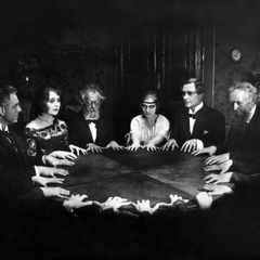 Schwarzweiß-Aufnahme von Menschen, die um einen Tisch sitzen und ihre Hände flach auf die Tischplatte gelegt haben