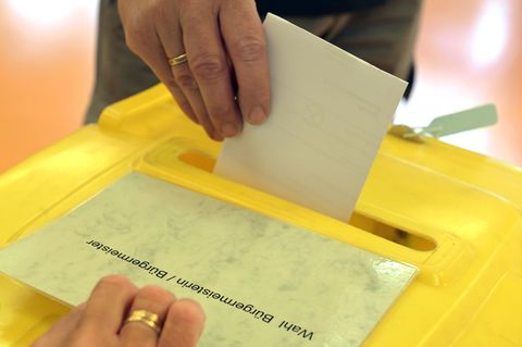 Ein Mann wirft einen Wahlzettel in die Urne zur Bürgermeisterwahl