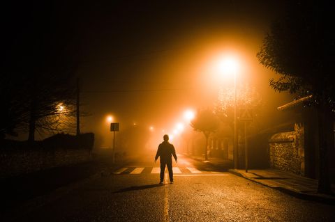 Ein Mann steht in einer dunklen Straße und wird von einer Straßenlampe düster beleuchtet. Hier ist Stadtplanung nötig.