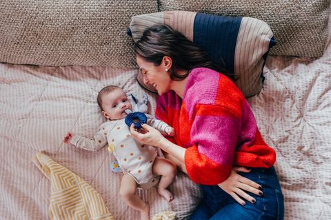 Eine Frau liegt mit ihrem Baby auf dem Boden und spielt