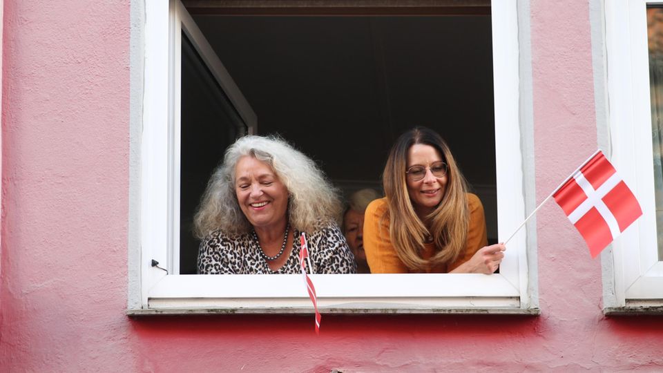 Zwei Frauen schauen aus einem Fenster und halten dänische Fahnen