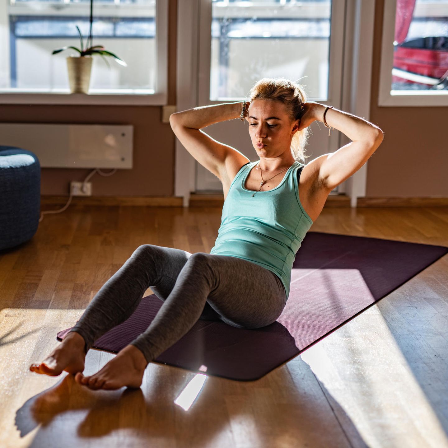 Eine Frau macht Sit-ups in ihrem Wohnzimmer. Sie liegt auf dem Boden und geht mit dem Oberkörper nach oben.