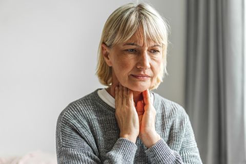 Frau fasst sich an den Hals