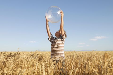 Kleiner Junge hält eine Weltkugel in die Luft, während er in einem freien Feld steht