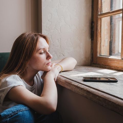 Eine Frau sitzt am Fenster und guckt auf ihr Handy