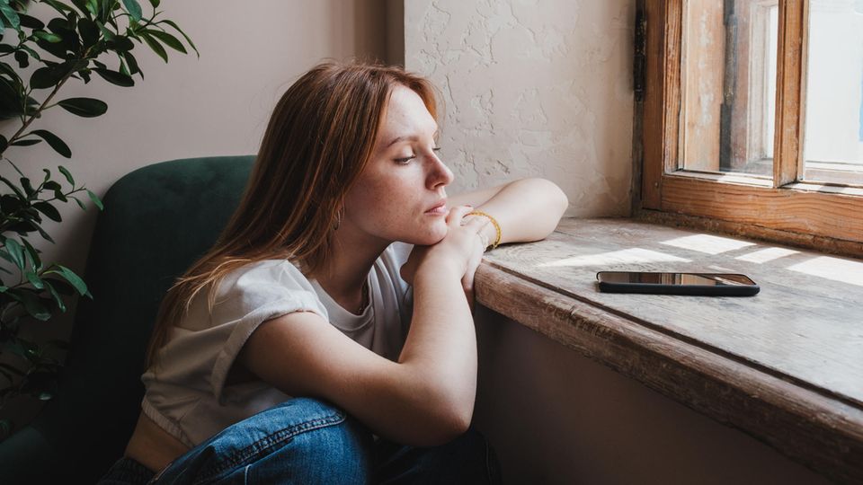 Eine Frau sitzt am Fenster und guckt auf ihr Handy