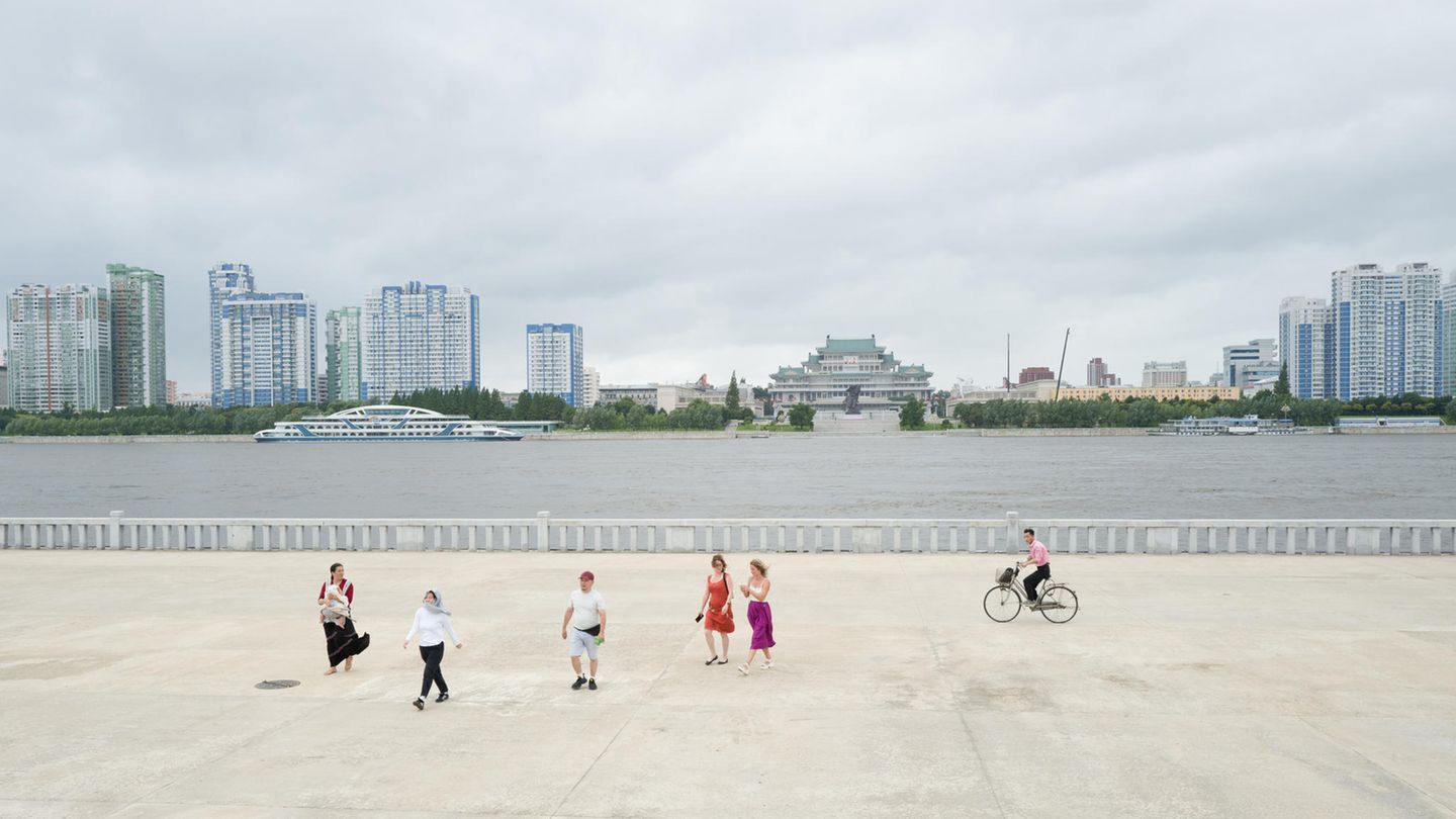 Fotografie: Nur ein Radfahrer ist unterwegs, als die russischen Touristen aus der Ferne auf den Kim Il-sung-Platz blicken: Der liegt auf der anderen Seite des Flusses. Unter dem aktuellen Diktator Kim Jong-un erlebte die Hauptstadt einen regelrechten Bauboom. Die meisten Nordkoreaner leben jedoch in bitterer Armut Nur ein Radfahrer ist unterwegs, als die russischen Touristen aus der Ferne auf den Kim Il-sung-Platz blicken: Der liegt auf der anderen Seite des Flusses. Unter dem aktuellen Diktator Kim Jong-un erlebte die Hauptstadt einen regelrechten Bauboom. Die meisten Nordkoreaner leben jedoch in bitterer Armut
