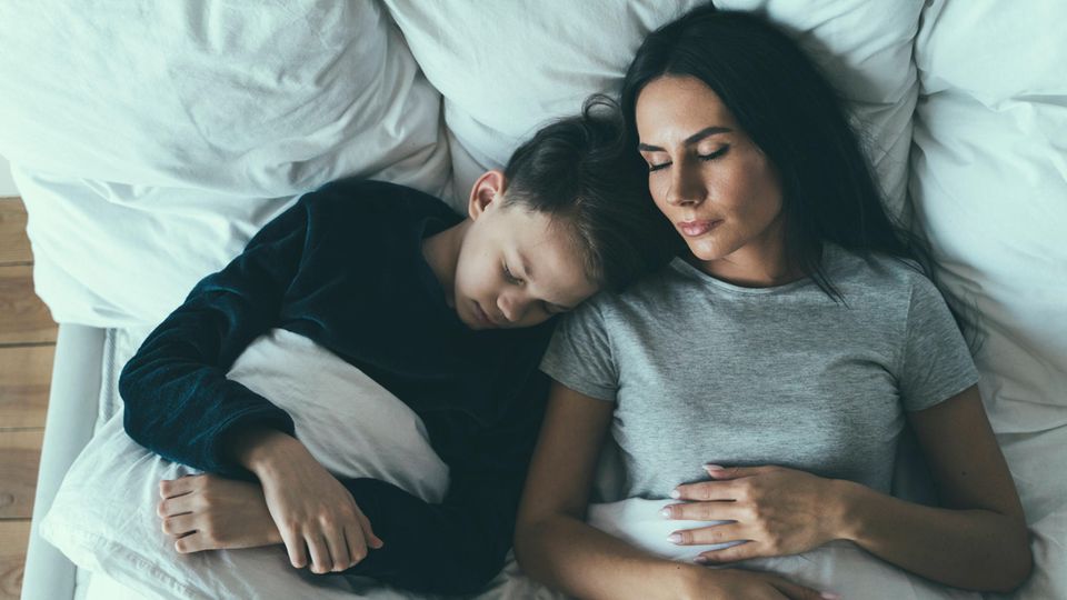 Zeitumstellung: Eine Mutter liegt mit ihrem Sohn im Bett und schläft