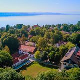 Hinter hohen Bäumen in der Nähe des Ufers liegt das Internat Landheim Ammersee.
