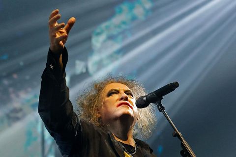 Robert Smith von The Cure reckt auf der Bühne den Arm in die Höhe