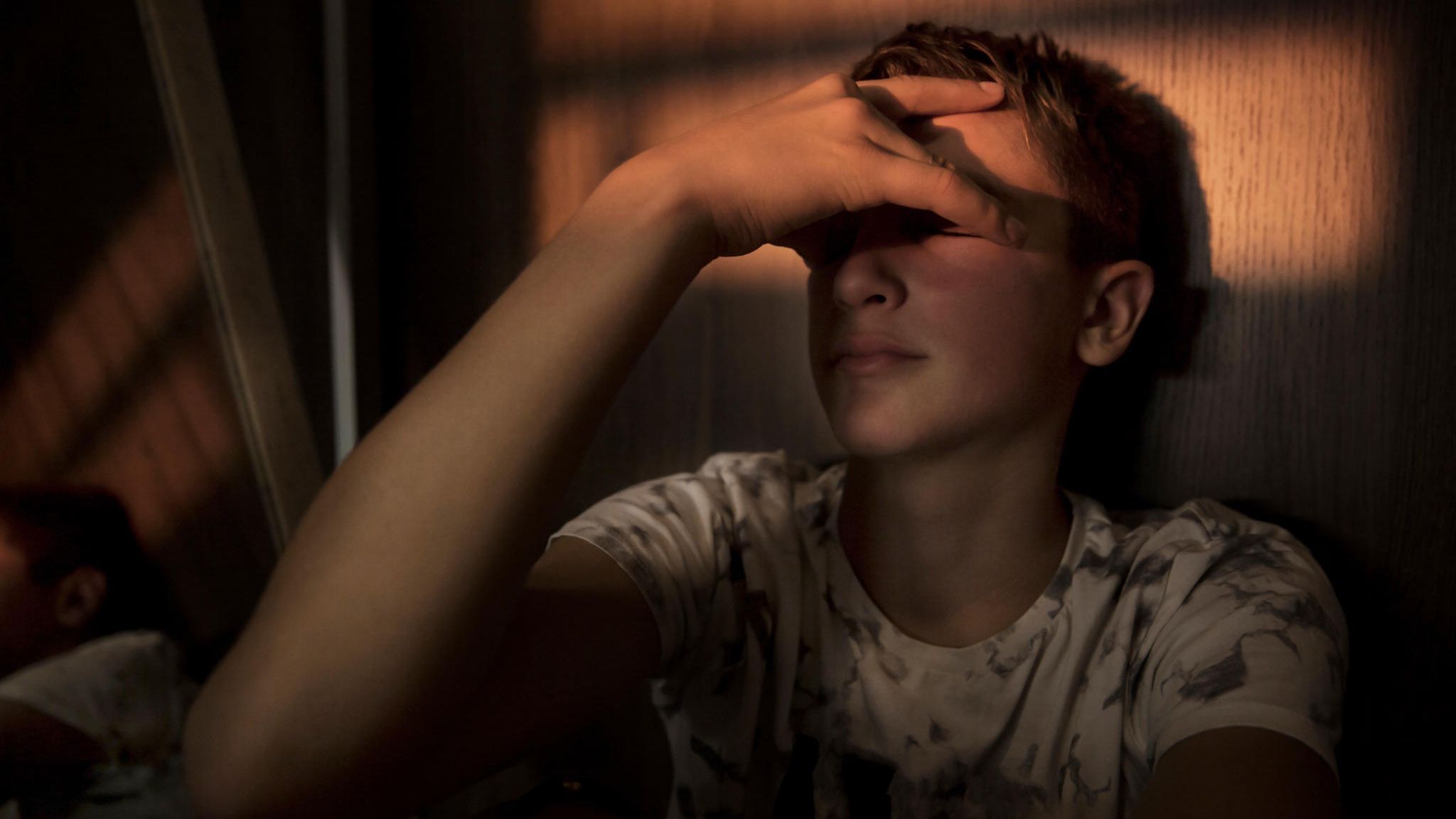 Gedanken an Suizid? Junger Mann hält sich verzweifelt die Hand vor die Augen