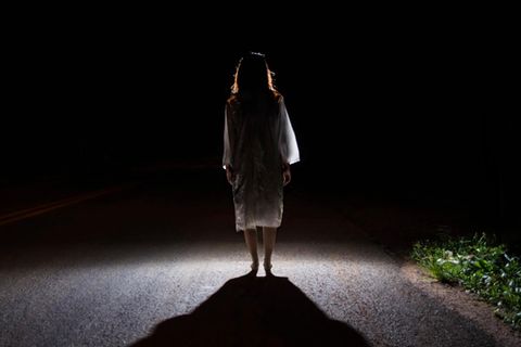 Eine Frau steht auf einer Straße, von hinten beleuchtet