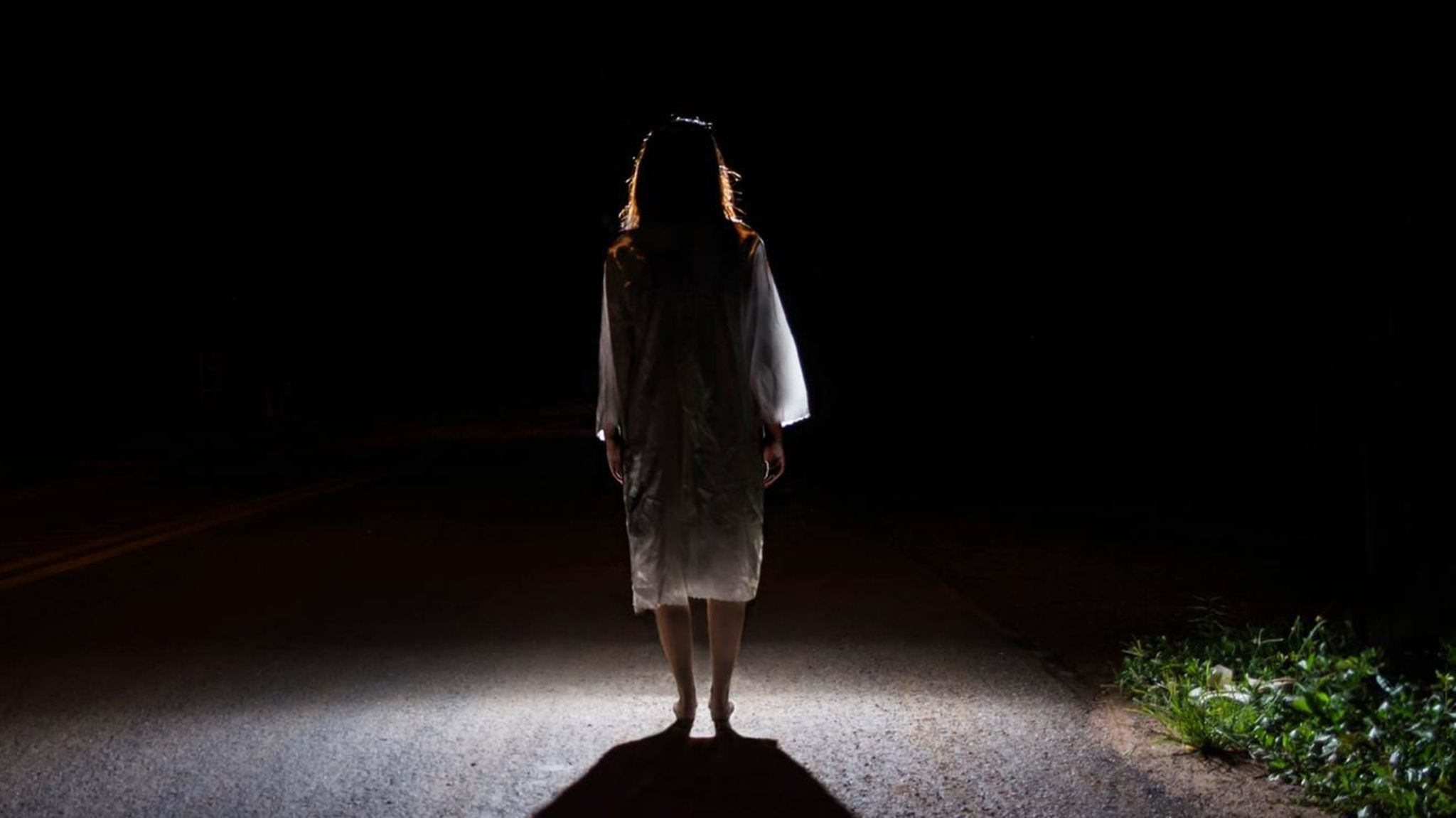 Eine Frau steht auf einer Straße, von hinten beleuchtet