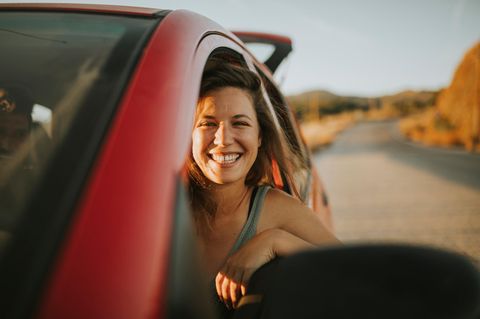 Auto mieten für den Urlaub: Frau schaut lachend aus einem Autofenster.
