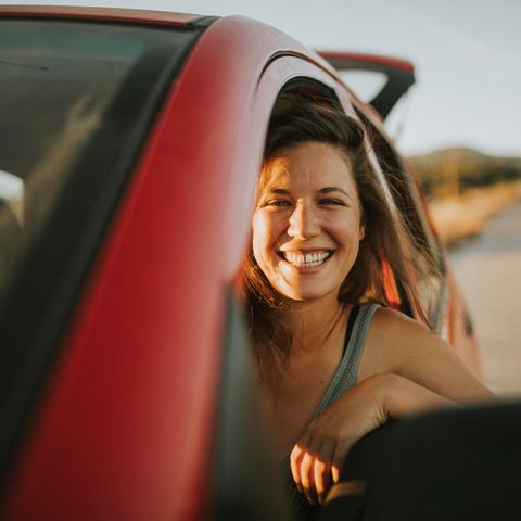 Auto mieten für den Urlaub: Frau schaut lachend aus einem Autofenster.
