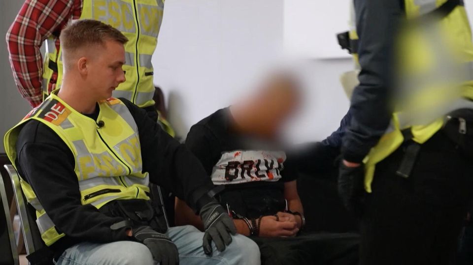 Polizist Cedric sitzt neben einem Flüchtling im Flughafen, es ist sein erster Einsatz