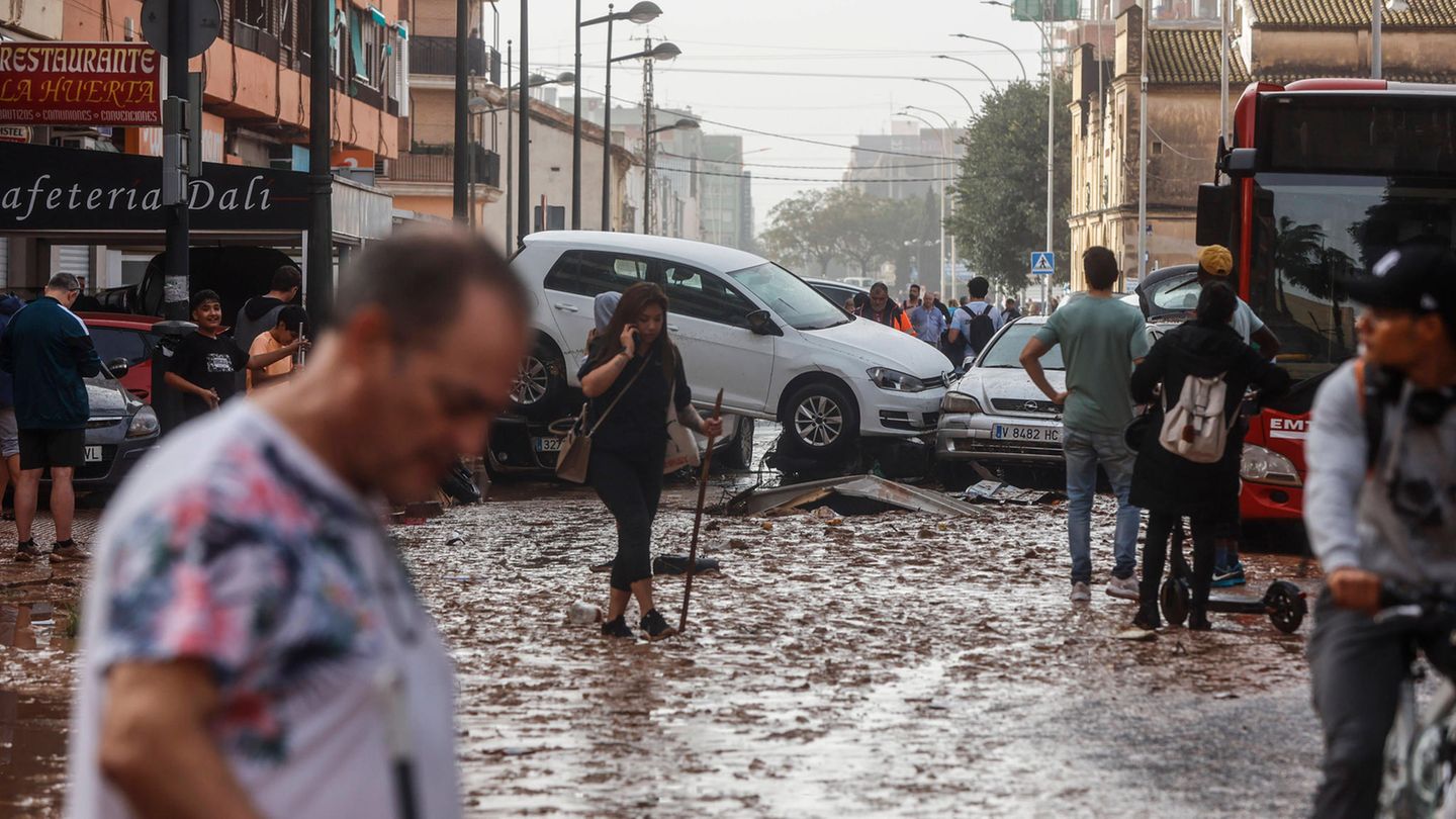 Menschen laufen durch das überflutete Valencia, Autos stapeln sich