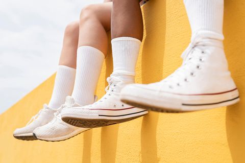 Beine mit langen weißen Socken hängen über einer gelben Mauer