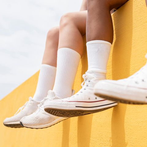 Beine mit langen weißen Socken hängen über einer gelben Mauer